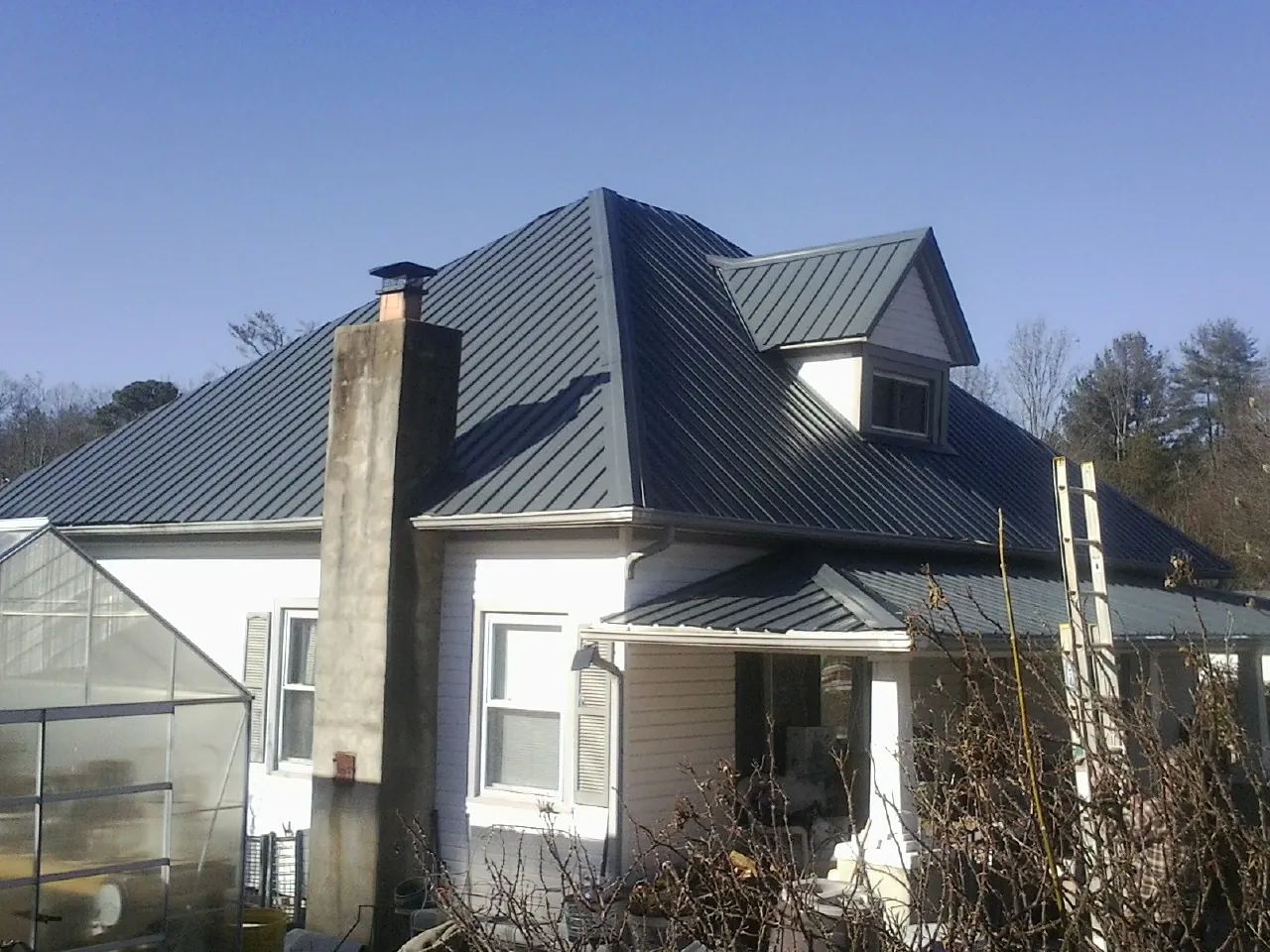 Dark blue standing seam metal roof on a white farmhouse with dormer — Slate & Tile Roof Repair by Roofing Brothers in Miles