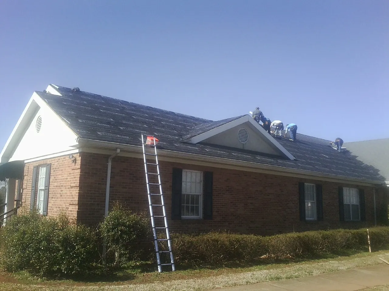 Crew tearing shingles off a brick ranch roof with a ladder set — Emergency Roof Repair work by our crew in Miles