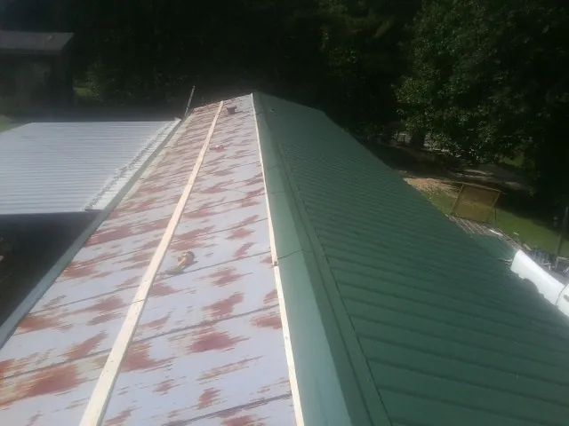 Old rusted panels beside newly installed green metal roofing — Wind Damage Roof Repair by Roofing Brothers in Miles