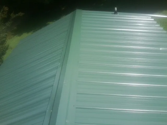 New green metal panels meeting at the ridge of a roof — Flat Roof Repair work by our crew in Miles
