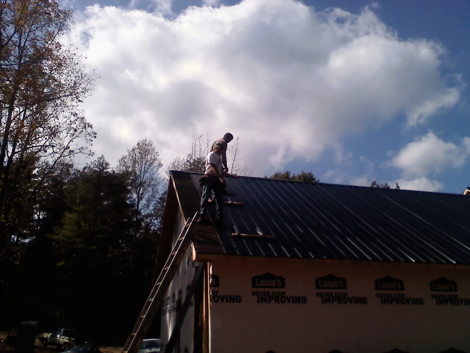 Roofer fastening dark metal panels high against a cloudy sky, from a Roof Inspection job in Miles