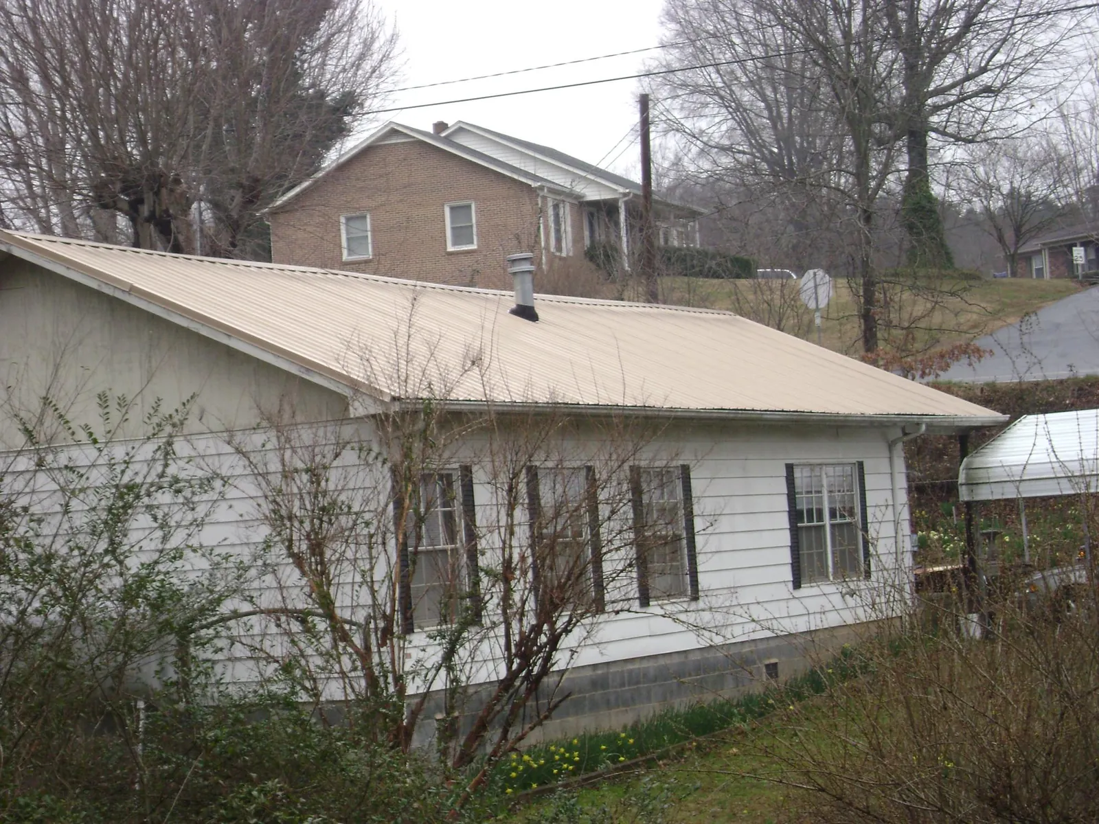 Tan metal roof on a white sided house set into a hillside — Commercial Roofing by Roofing Brothers in Miles